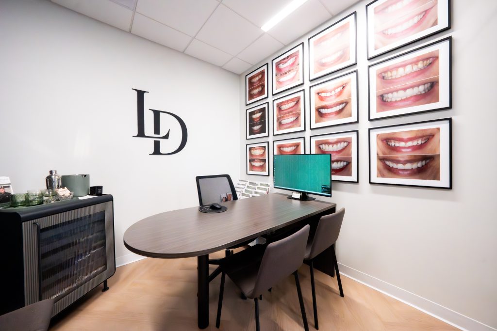 Limitless Dental consultation room in Jersey City with the smile gallery wall of twelve framed before-and-after smile photos behind an oval consult table.