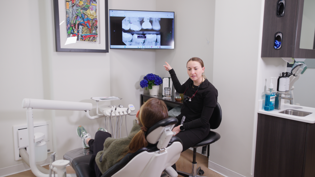 Dr. Nick Ciardiello pointing at a Pearl AI-annotated dental x-ray on a chairside monitor while reviewing findings with a reclined patient at Limitless Dental in Jersey City.