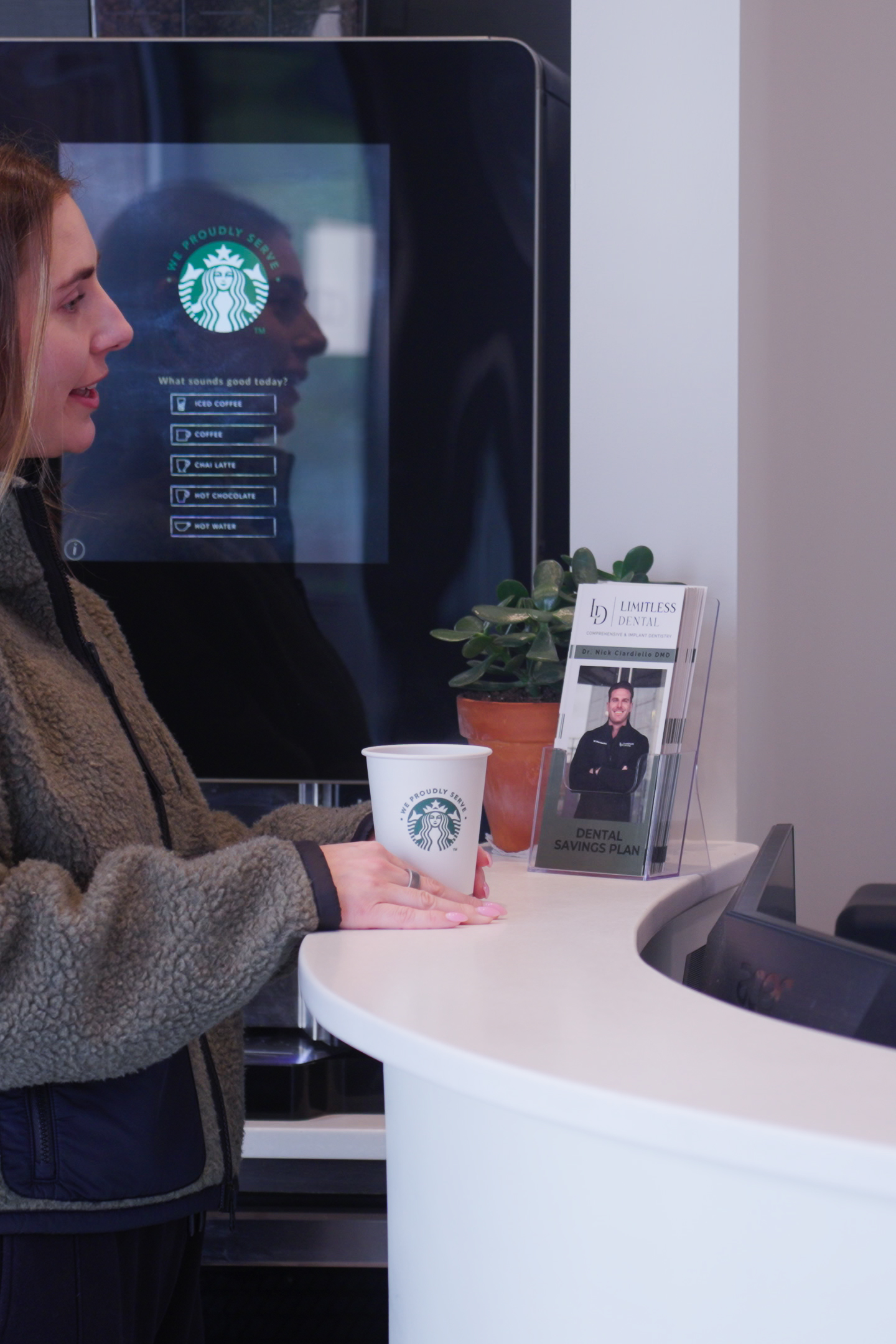A patient at Limitless Dental in Jersey City holding a Starbucks coffee cup while chatting with the receptionist at the front desk, showing the comfort amenities offered to help patients with dental anxiety feel welcome.