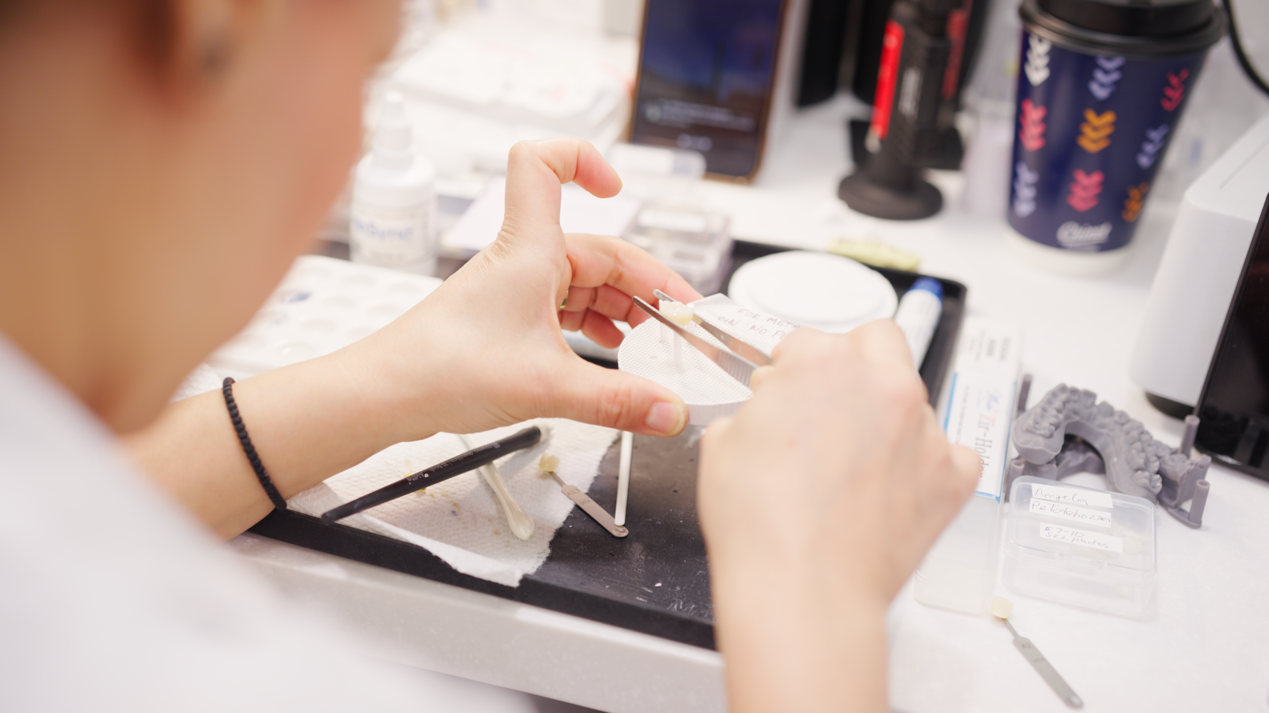 Dental team member at Limitless Dental in Jersey City holding a clear aligner tray with tweezers alongside dental models used for Invisalign treatment planning.