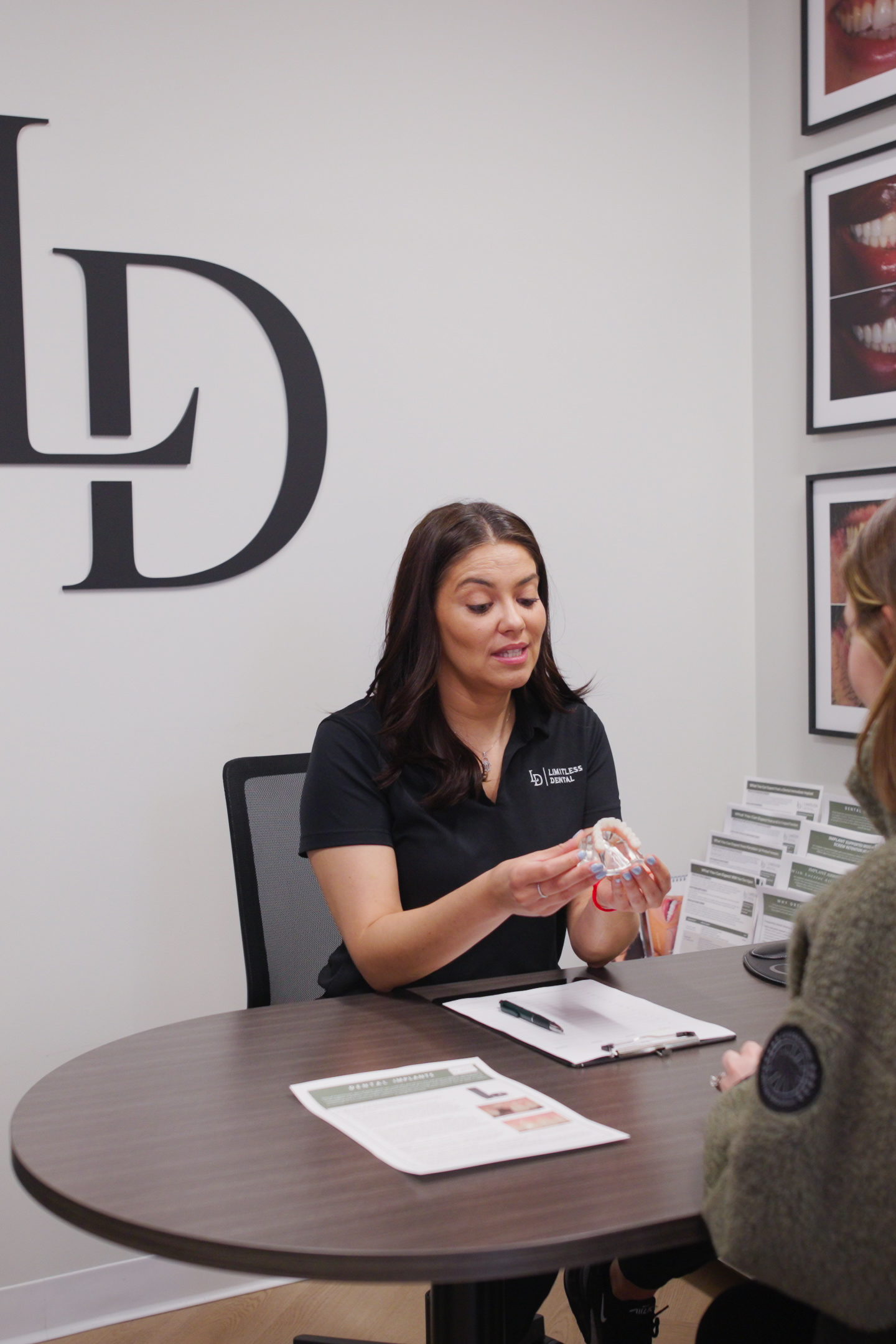 Limitless Dental coordinator holding a dental implant model while explaining implant versus denture options to a patient in Jersey City